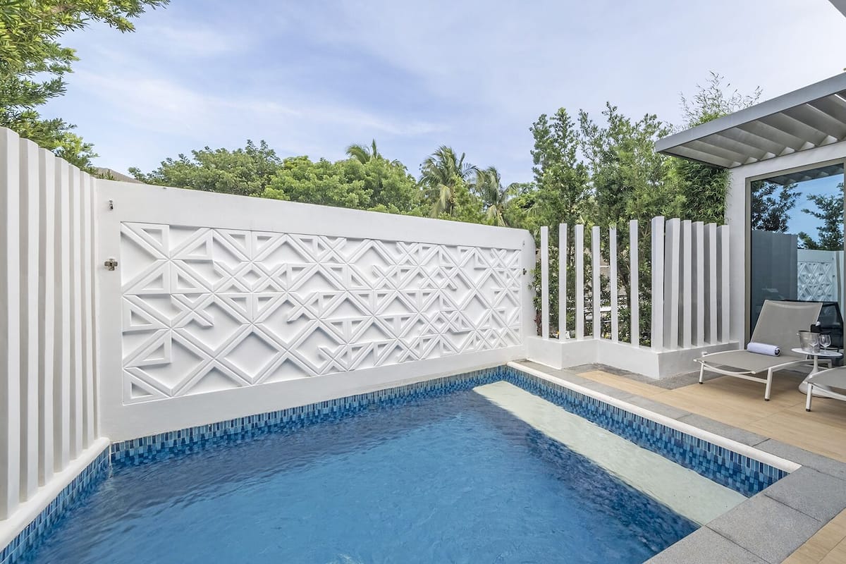 Un espace piscine extérieur moderne, agrémenté d’un mur au design géométrique, de chaises longues et d’une pergola.