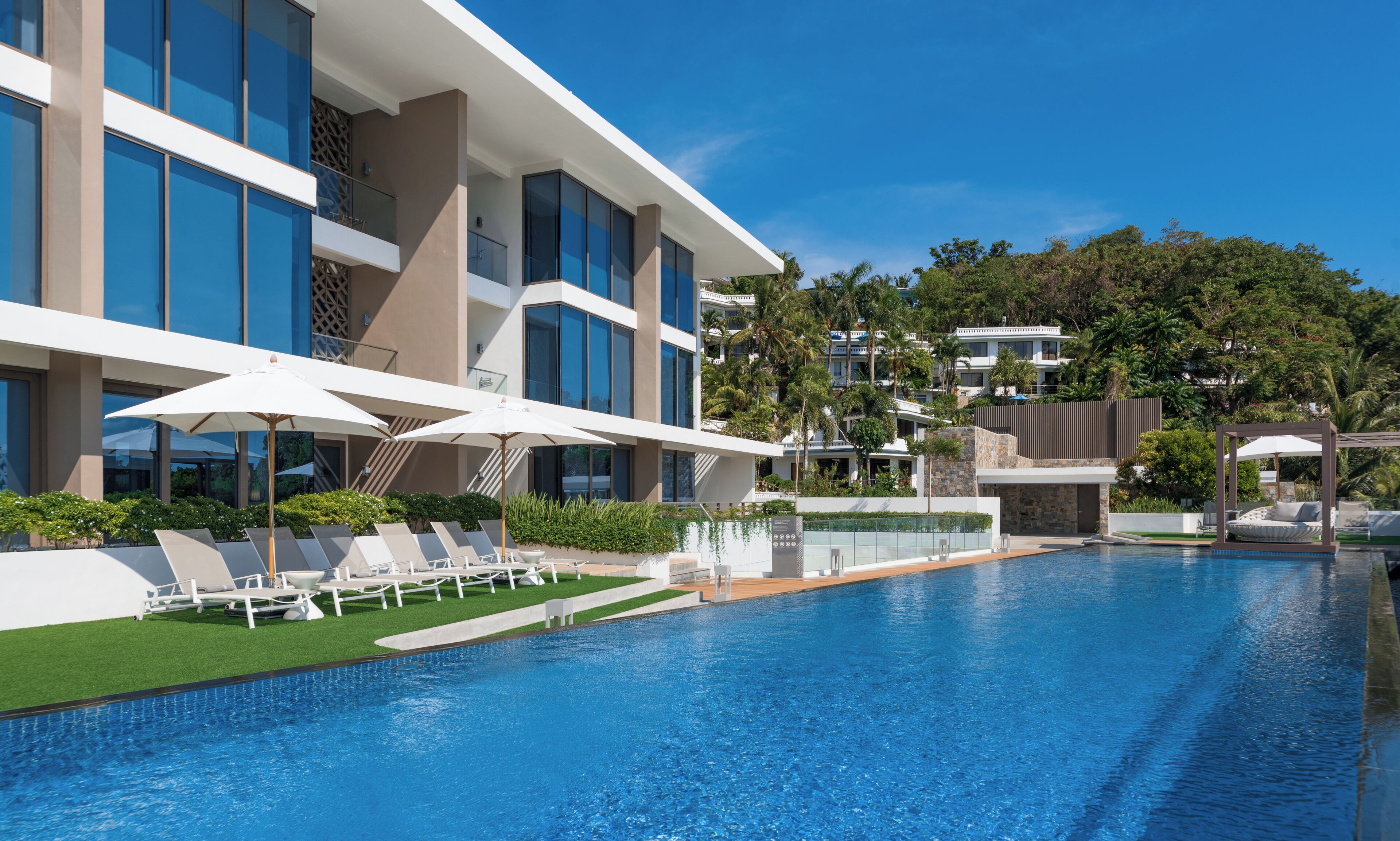 A modern hotel with a swimming pool, sun loungers, and umbrellas.