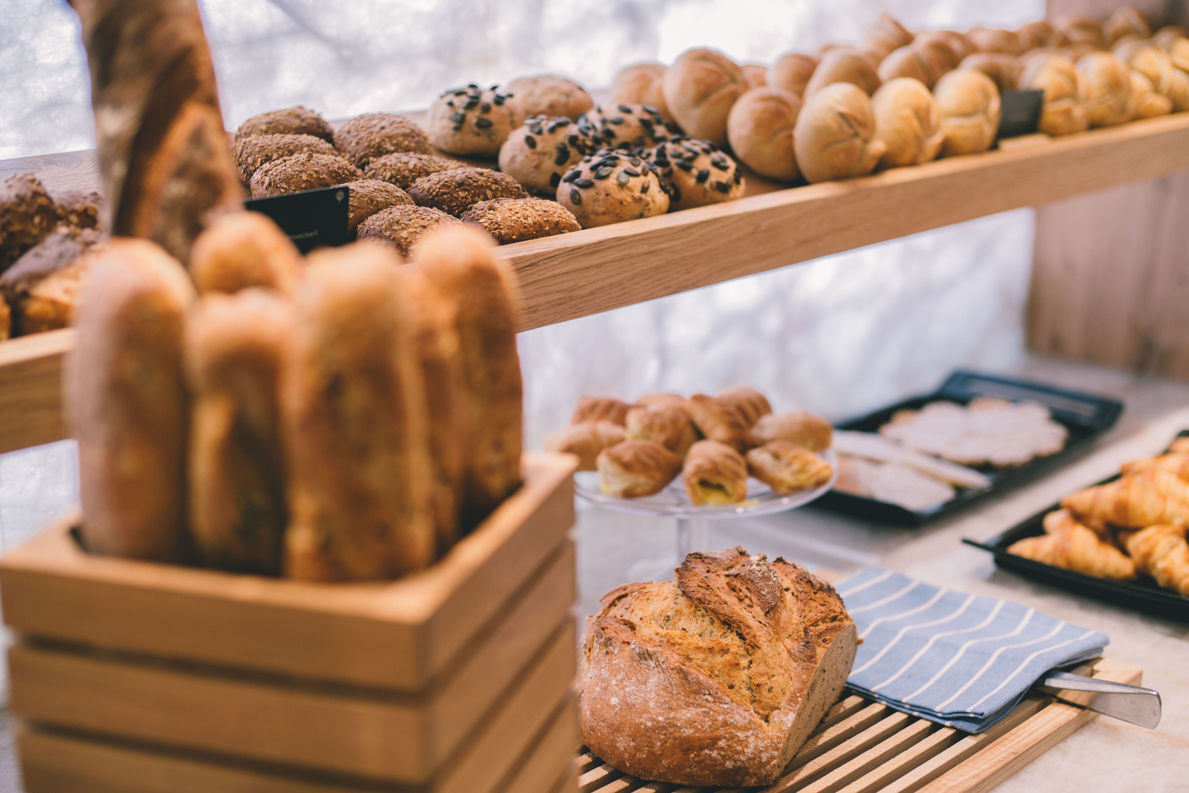 Une variété de produits de boulangerie présentés sur des étagères en bois, notamment des pains, des petits pains et des pâtisseries.