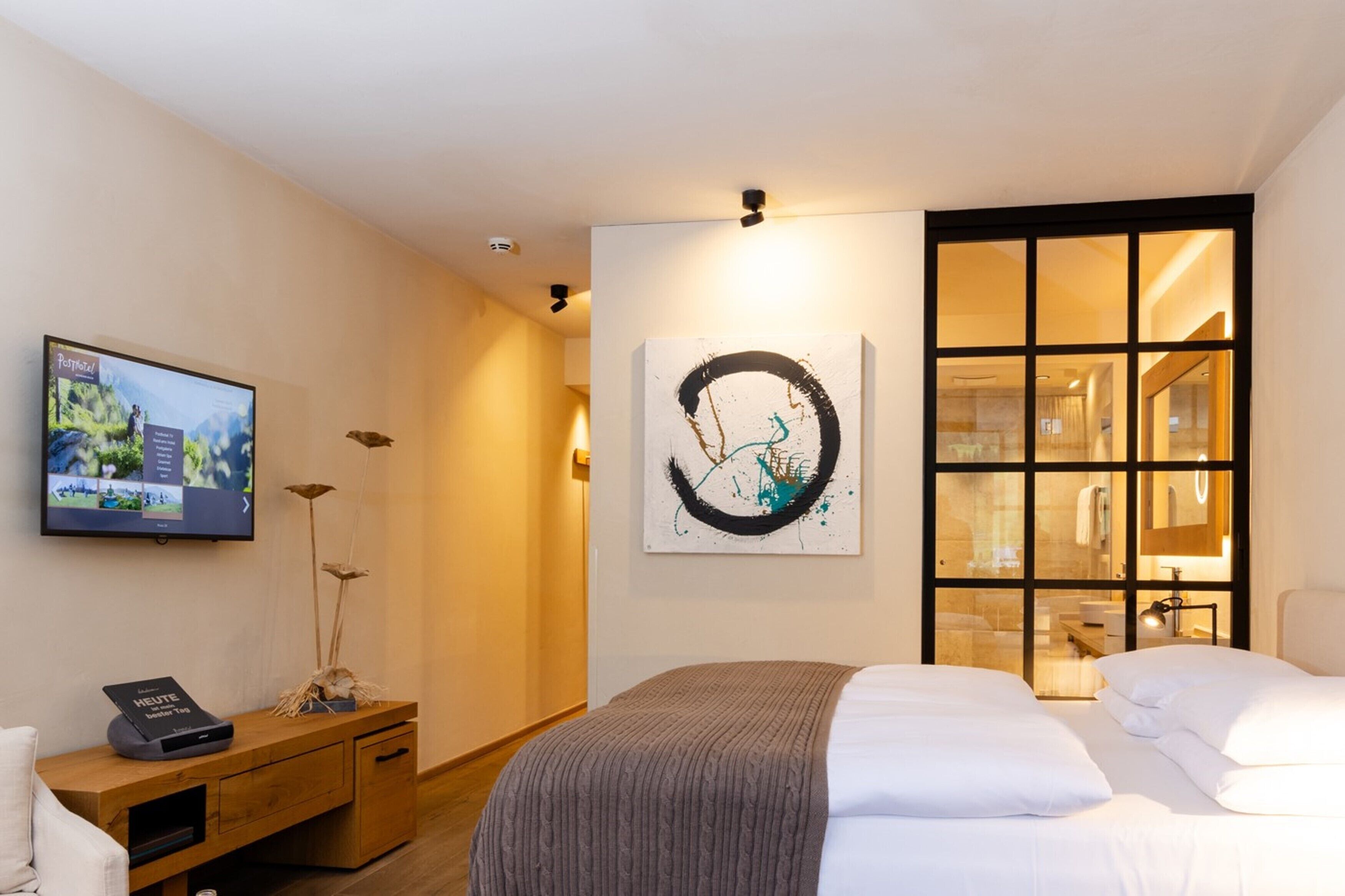 Habitación de hotel con cama, escritorio con ordenador, televisión y cuadros en la pared.