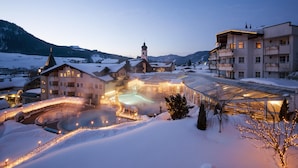 A hotel with a large glass greenhouse, a swimming pool, and a church in the background. - Posthotel Achenkirch Resort and Spa - Adults Only (Achenkirch)