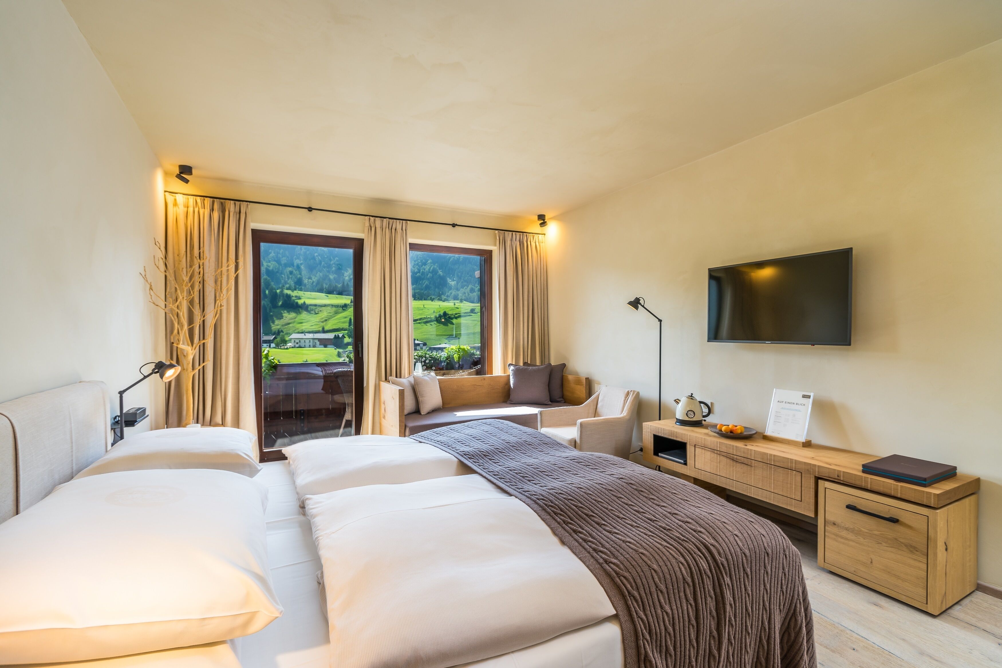 A hotel room with a large bed, a desk, a TV, and a view of a green landscape.