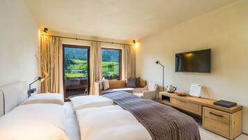A hotel room with a large bed, a desk, a TV, and a view of a green landscape.