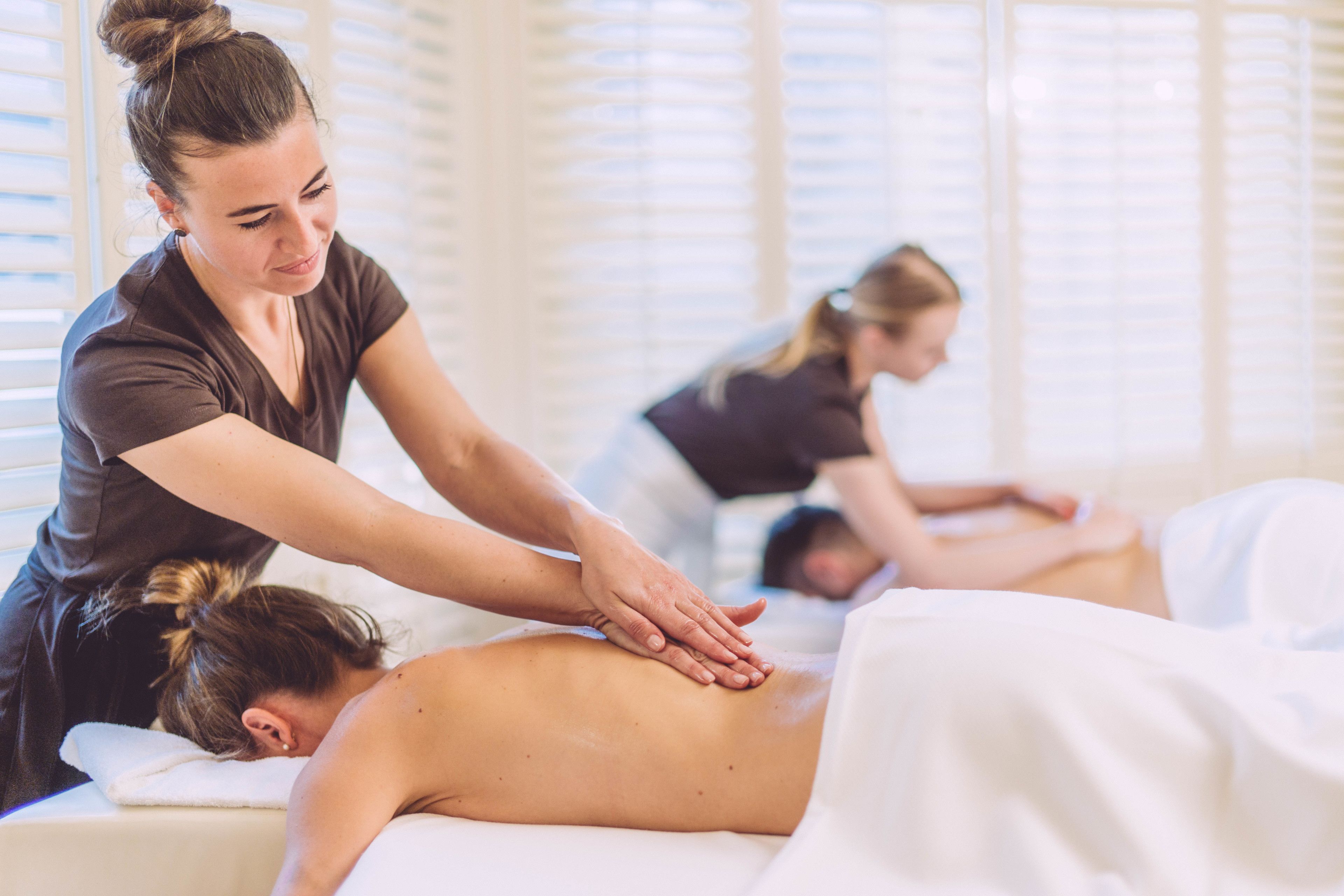Eine Massageanwendung in einem Raum mit weißen Betten und Jalousien.