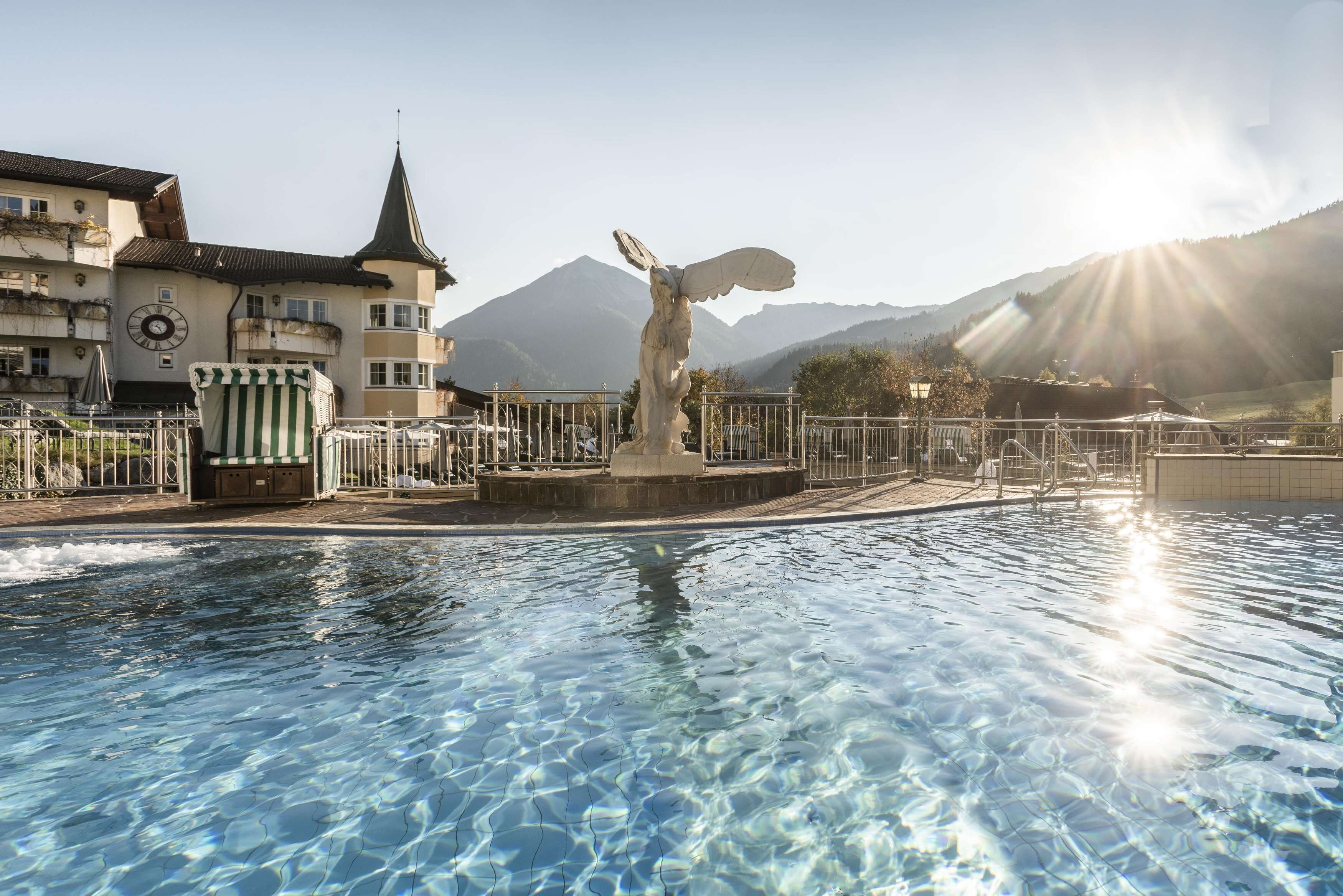 A swimming pool with a statue, a clock, and a building with a spire in the background.