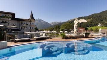 A swimming pool with a decorative fountain, outdoor seating, and a mountain backdrop.