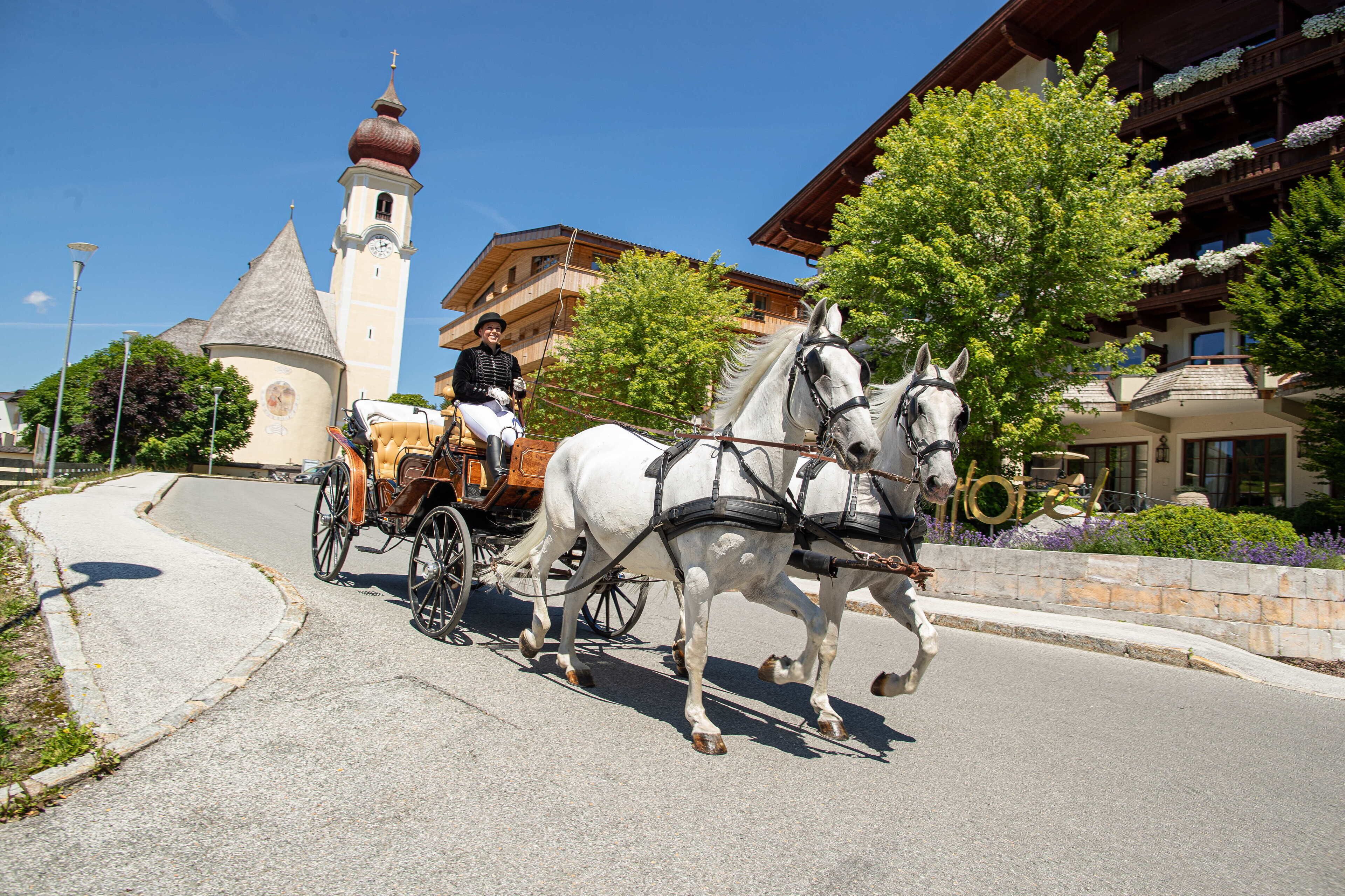 A horse-drawn carriage with a driver, a church with a clock tower, and a building with balconies.