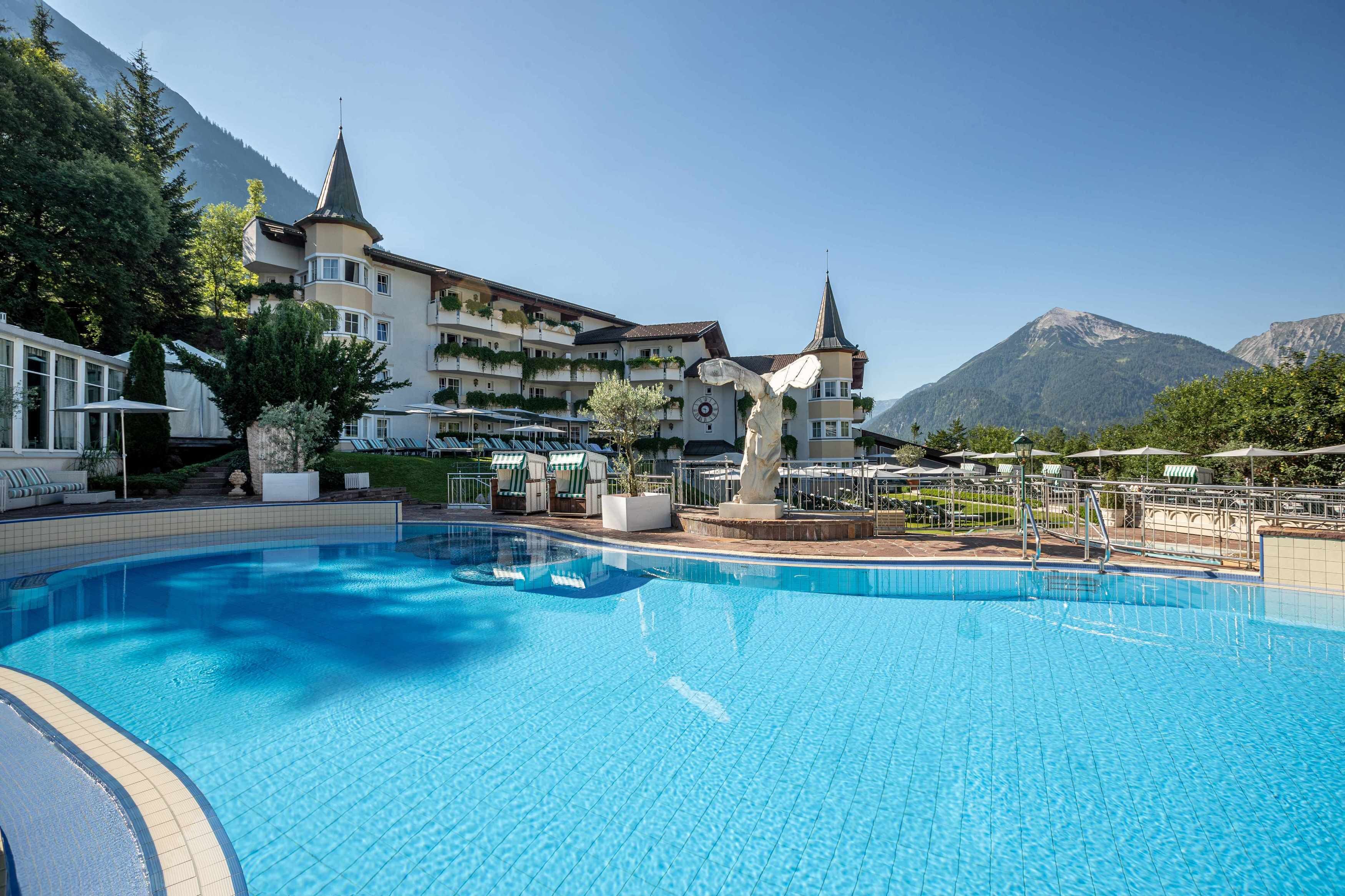 A swimming pool with a view of a mountain and a hotel building with multiple balconies and a clock tower.