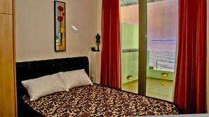 A bedroom with a bed, a painting, and a balcony with red curtains. - Beach Front Villa Peri (Hersonissos)