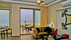 A room with a sofa, a coffee table, and a dining area with a table and chairs. There is a view of the sea through a glass door. - Beach Front Villa Peri (Hersonissos)