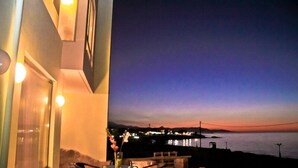 An outdoor seating area with a table and chairs, overlooking a body of water and a distant cityscape during twilight. - Beach Front Villa Peri (Hersonissos)