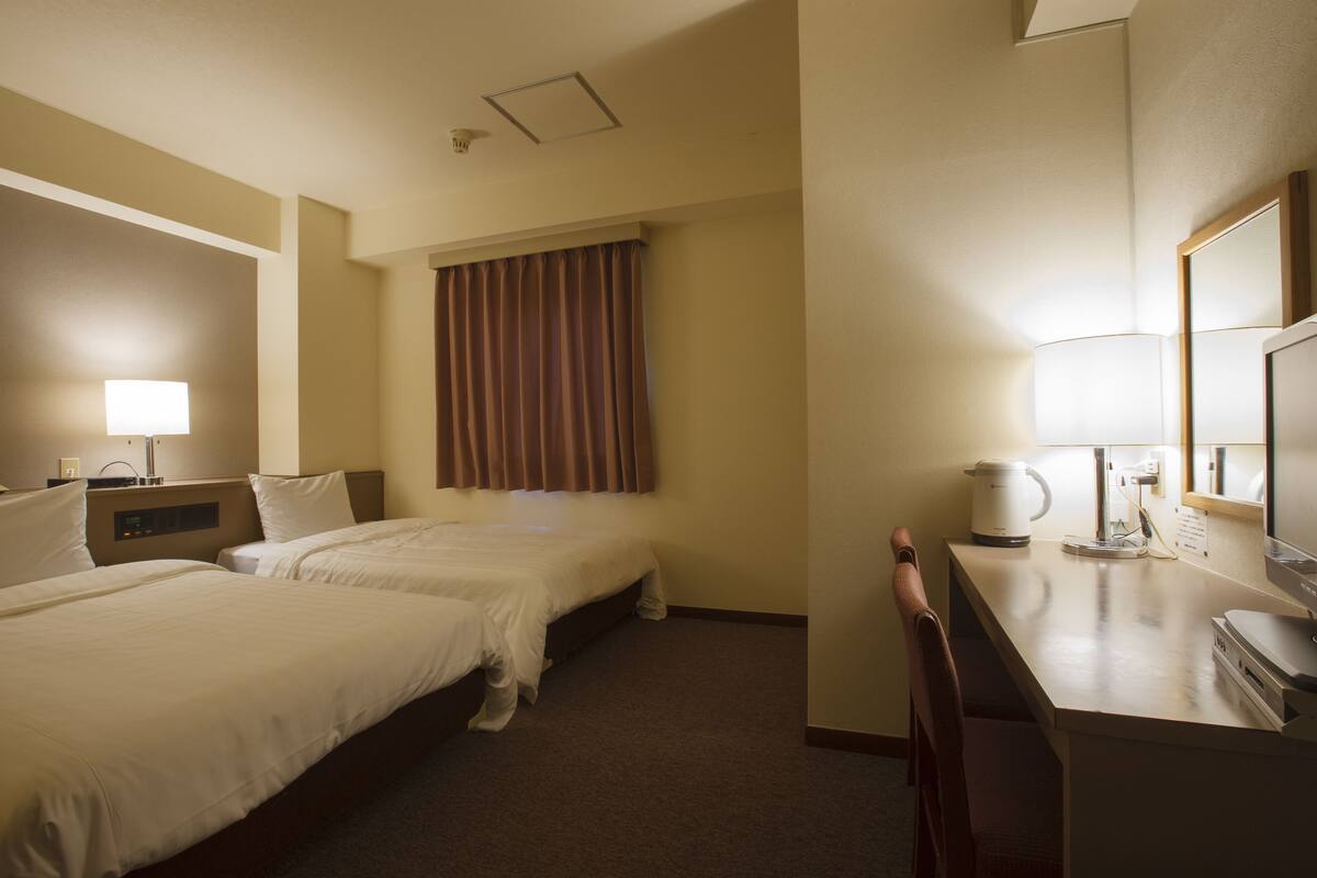 A hotel room with two beds, a desk with a coffee maker, a TV, and a window with curtains.