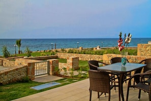 An outdoor patio with stone walls, a table with chairs, and a view of the sea. - Beach Front Villa Katrin (Hersonissos)