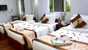 A hotel room with two beds, each with a brown headboard, white bedding, and rose petals scattered on the beds. There is a TV mounted on the wall, a small table with a vase of flowers, and a window with curtains. - Landmark Hotel (Yangon)