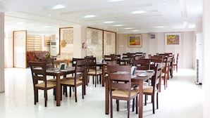 A spacious dining area with multiple wooden tables and chairs, a decorative partition, and a ceiling with recessed lighting. - Landmark Hotel (Yangon)