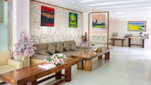 A modern hotel lobby with a wooden reception desk, a sofa, and a decorative wall with artwork. - Landmark Hotel (Yangon)