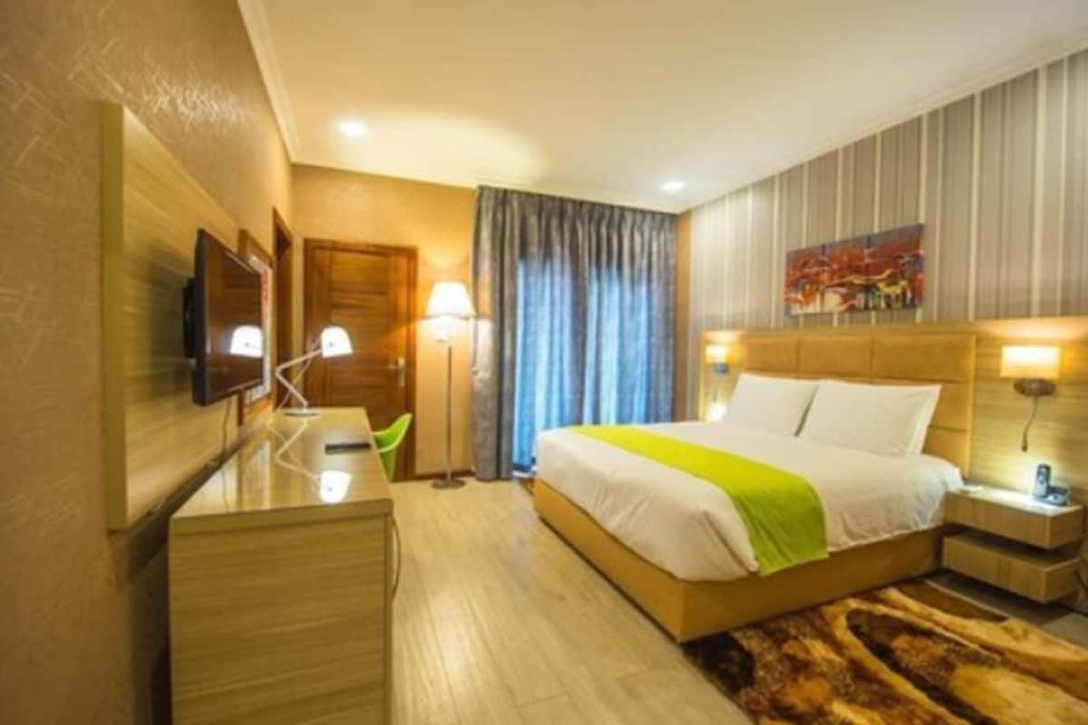 Une chambre d’hôtel avec un lit, des tables de chevet, un bureau, une télévision et un tableau au mur.