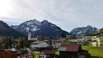Un village de montagne aux maisons traditionnelles, avec une église et des montagnes enneigées en toile de fond.