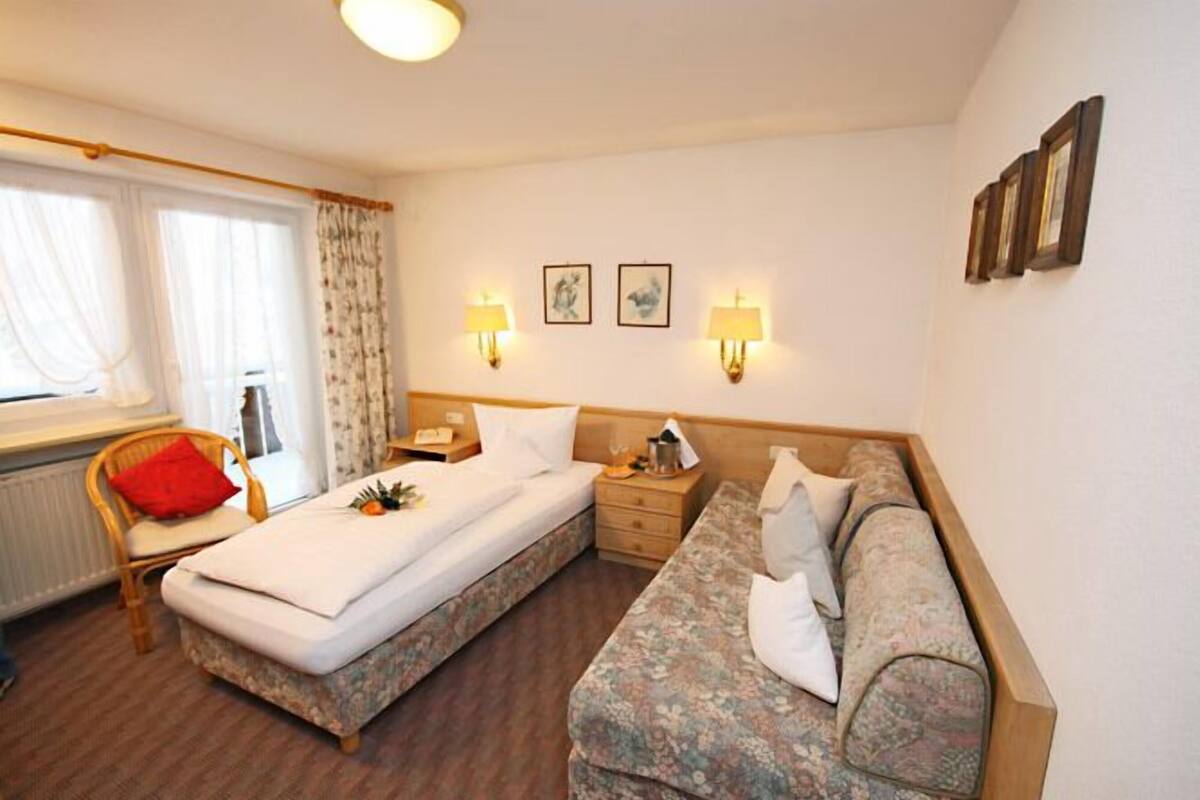 A hotel room with a bed, a sofa, a chair, and a nightstand.