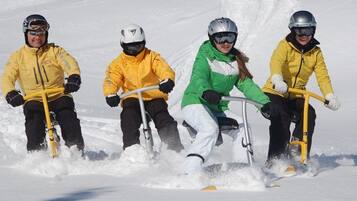 Vier Personen fahren mit Schneemobil auf einem verschneiten Weg.