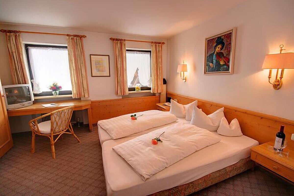 A hotel room with two beds, a desk, a chair, a television, and a painting on the wall.