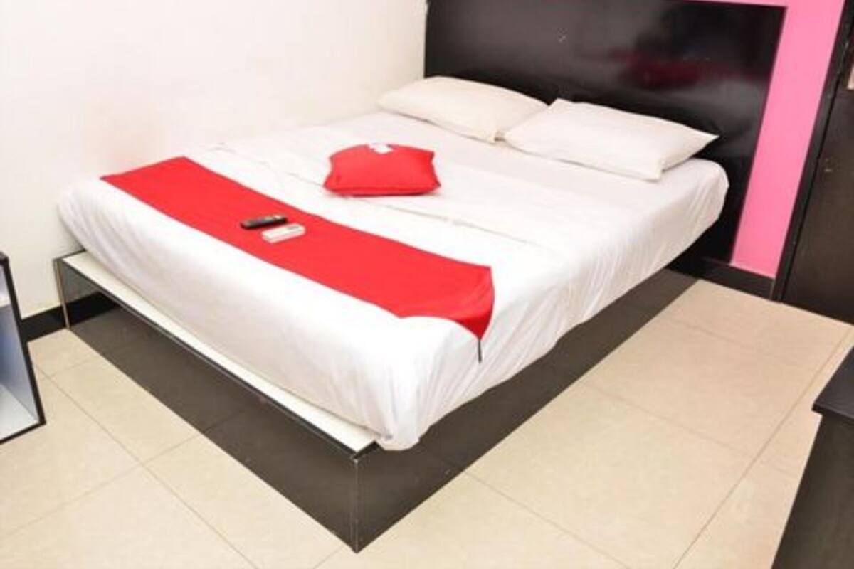 Ein Bett mit weißer Bettwäsche, einer roten Decke, einem schwarzen Kopfteil und einem weißen Kissen.