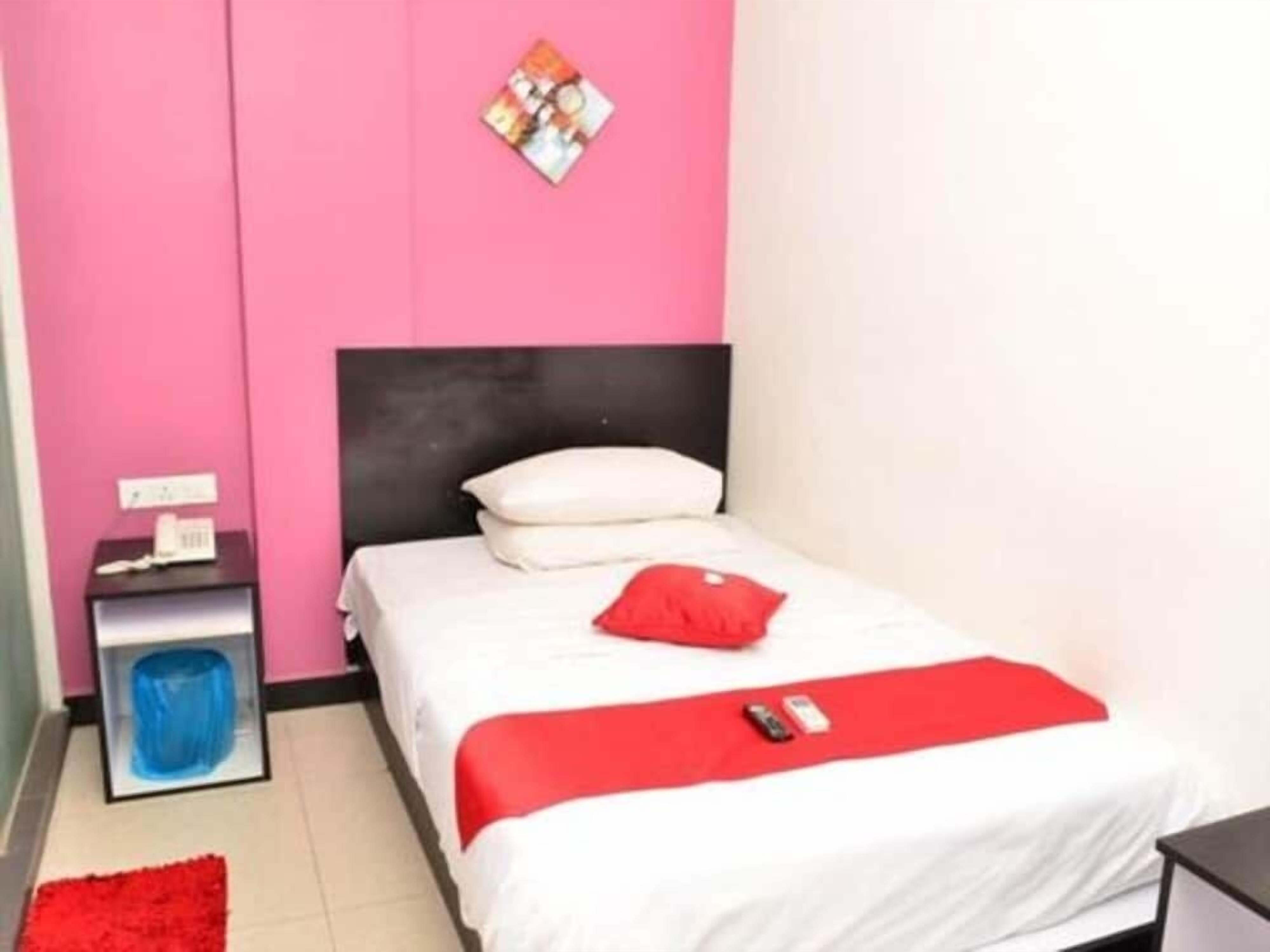 Een slaapkamer met een bed, nachtkastje, rode plaid en een aan de muur hangend schilderij.