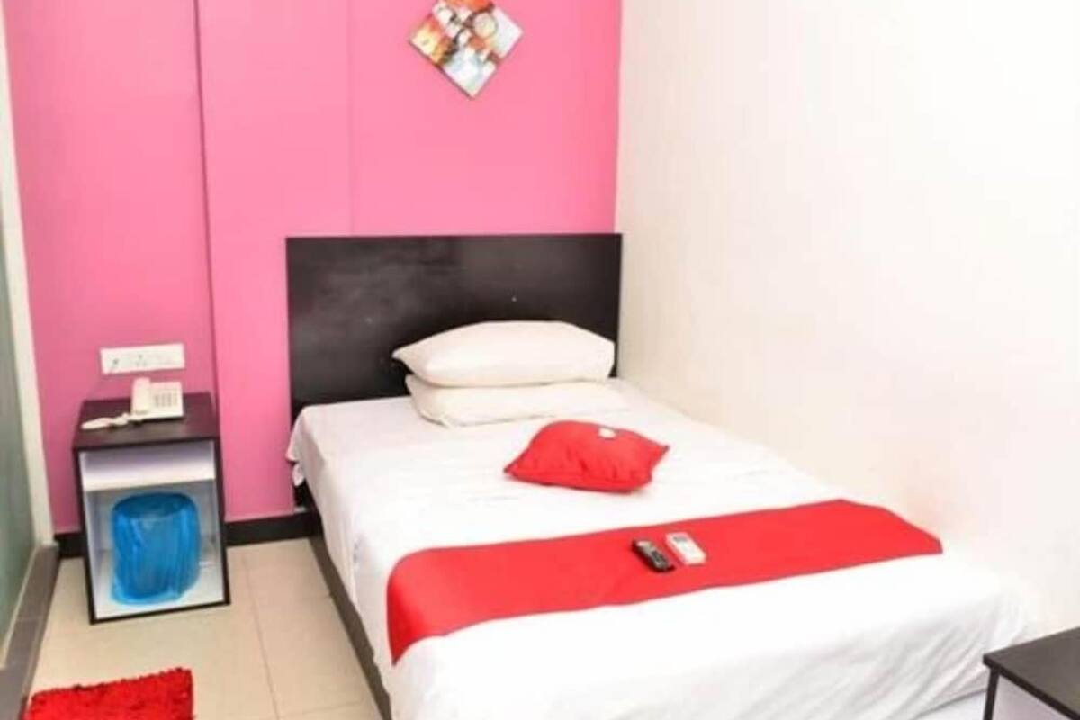 Un dormitorio con cama, mesita de noche, plaid rojo y un cuadro colgado en la pared.