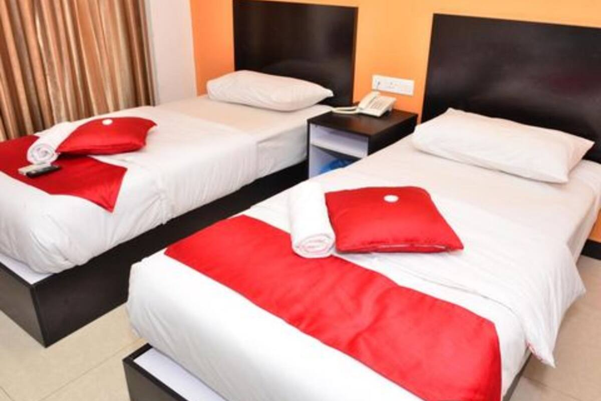 Ein Hotelzimmer mit zwei Betten, jeweils mit weißer Bettwäsche und roten Akzenten. Zwischen den Betten befindet sich ein Nachttisch mit Telefon und Lampe.