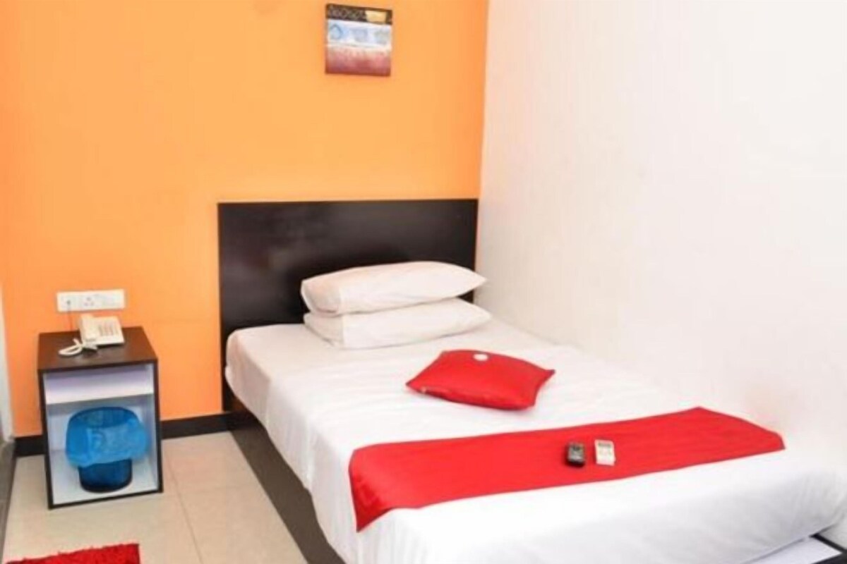 A hotel room with a bed, a nightstand with a phone, a red pillow, and a red blanket.