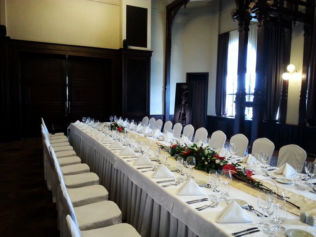 A long dining table set for a formal event, with white chairs and a floral centerpiece.