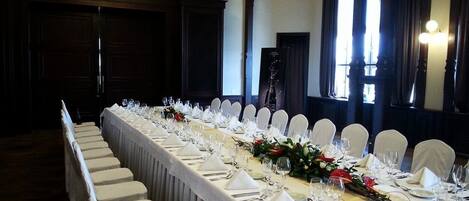 A long dining table set for a formal event, with white chairs and a floral centerpiece.
