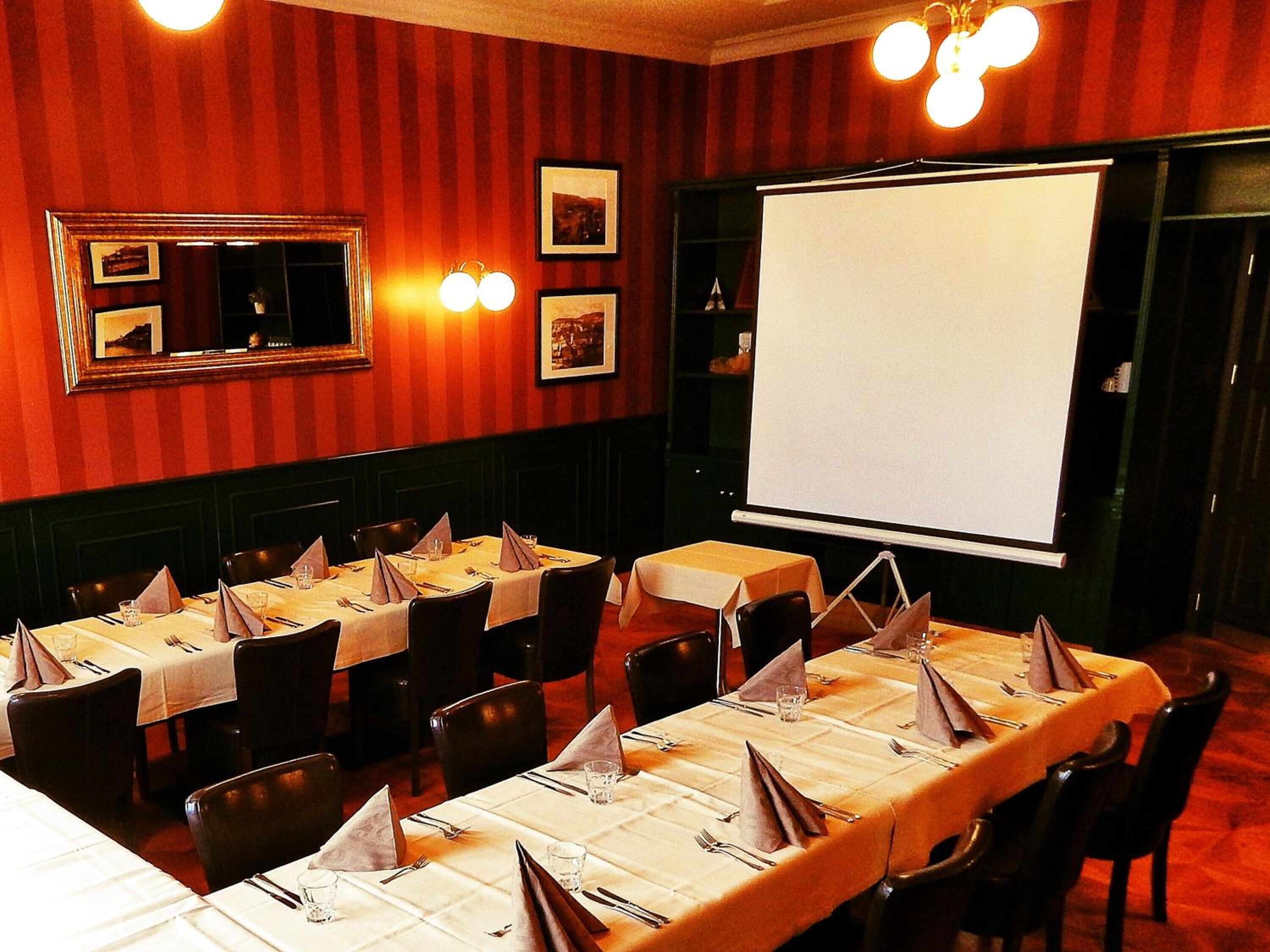 A restaurant with tables set for dining, a projection screen, and framed pictures on the wall.