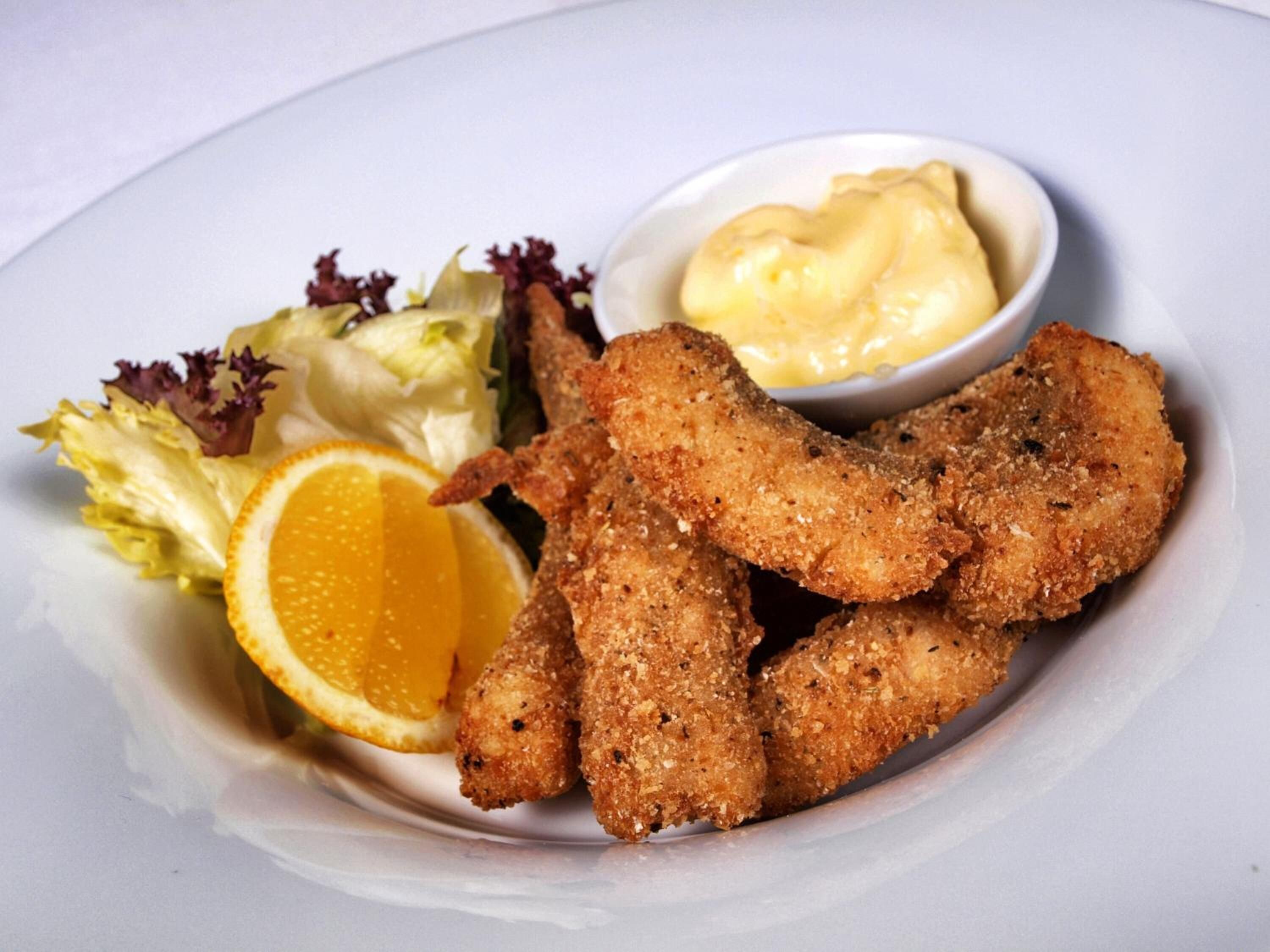 Une assiette contenant des aliments panés et frits, une tranche d’orange, de la laitue et un petit bol de sauce.