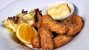 Une assiette contenant des aliments panés et frits, une tranche d’orange, de la laitue et un petit bol de sauce.