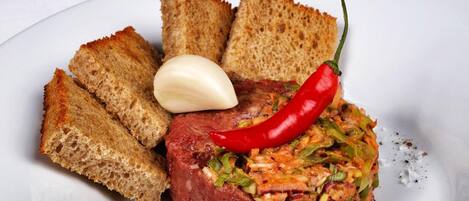 Ein Teller mit einem Fleischgericht, einer roten Chilischote, einer Knoblauchzehe und geröstetem Brot.
