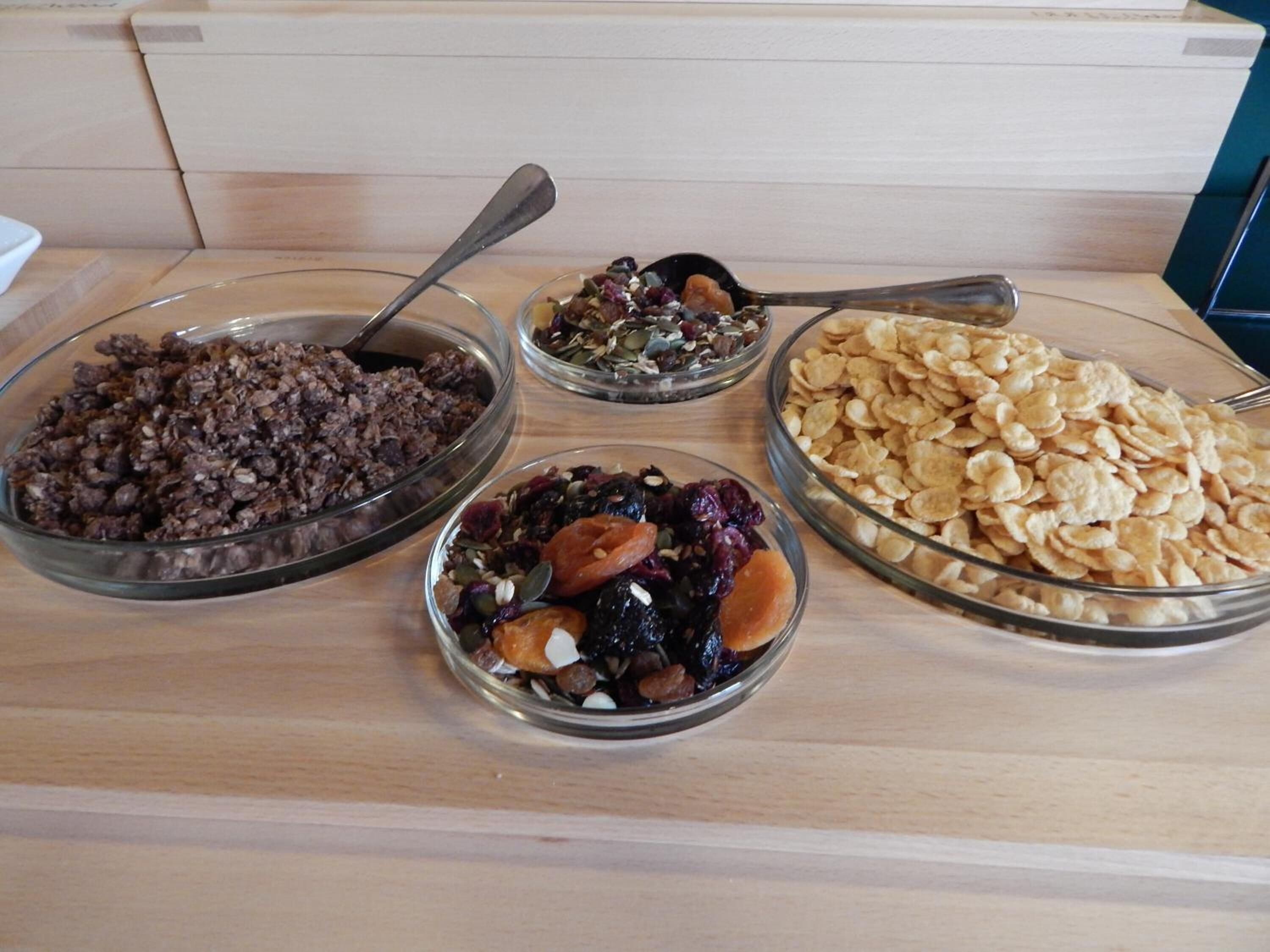 Una mesa de buffet con cuatro recipientes de vidrio que contienen diferentes tipos de comida.