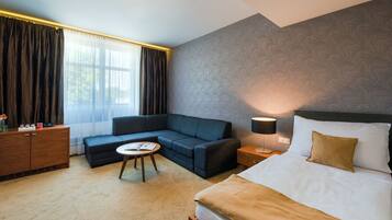 Une chambre d’hôtel avec un lit, un canapé, une petite table et une table de chevet avec une lampe.