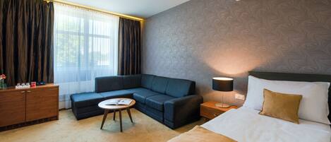 Ein Hotelzimmer mit Bett, Sofa, kleinem Tisch und Nachttisch mit Lampe.