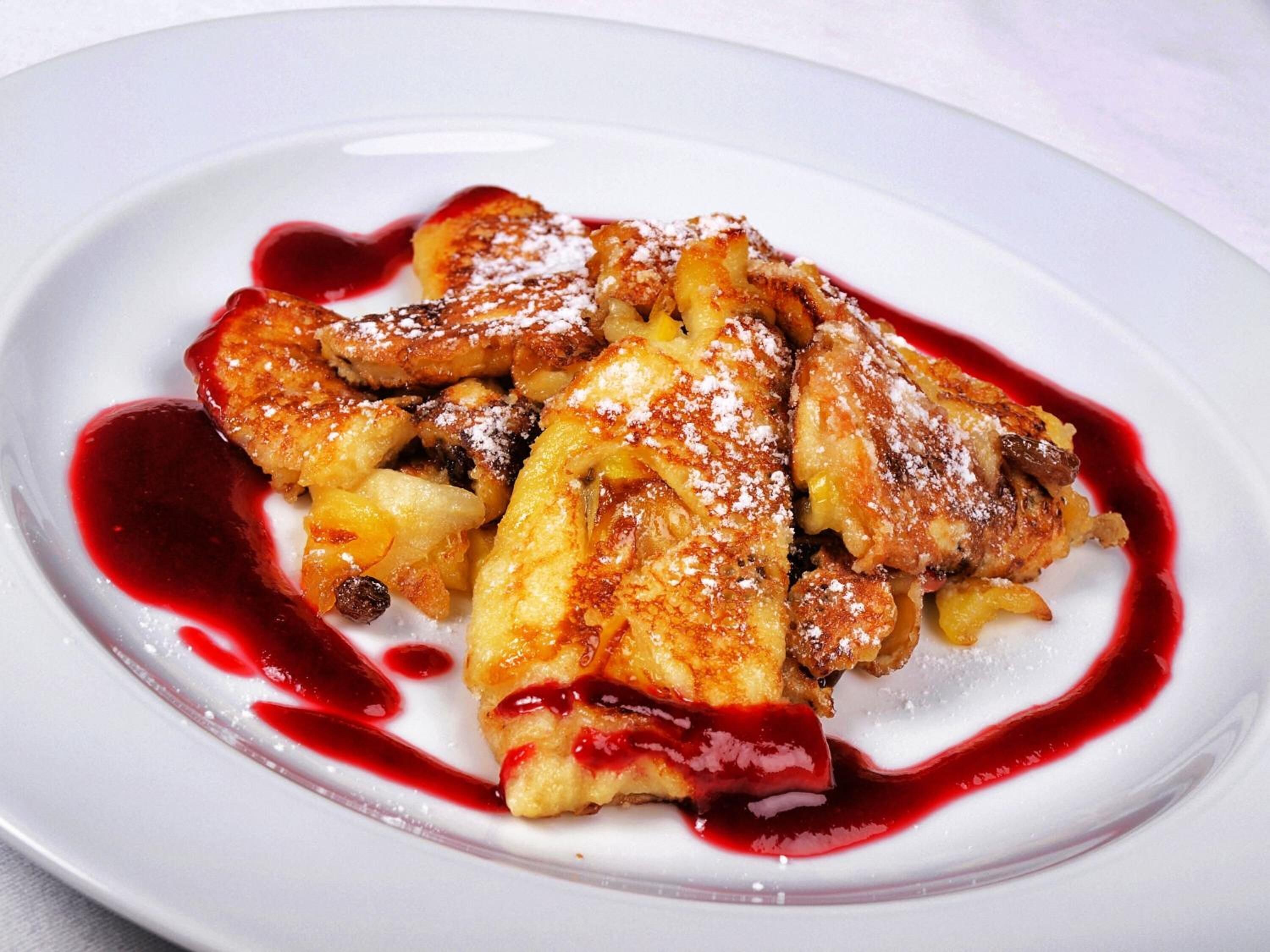 Un piatto dessert con un dolce al forno, probabilmente un budino di pane, cosparso di zucchero a velo e circondato da salsa rossa.
