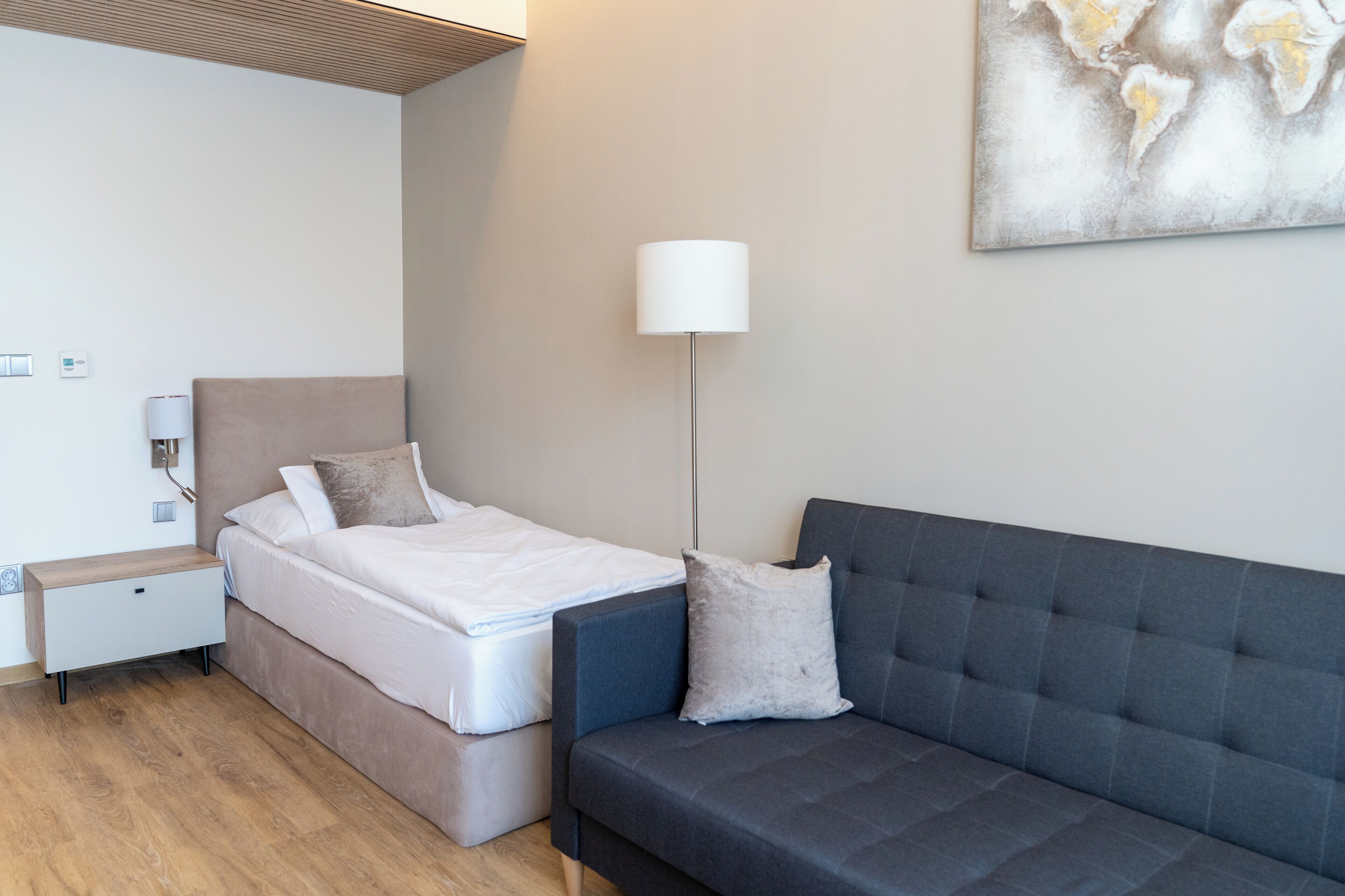 A modern bedroom with a bed, a nightstand, a lamp, and a sofa.