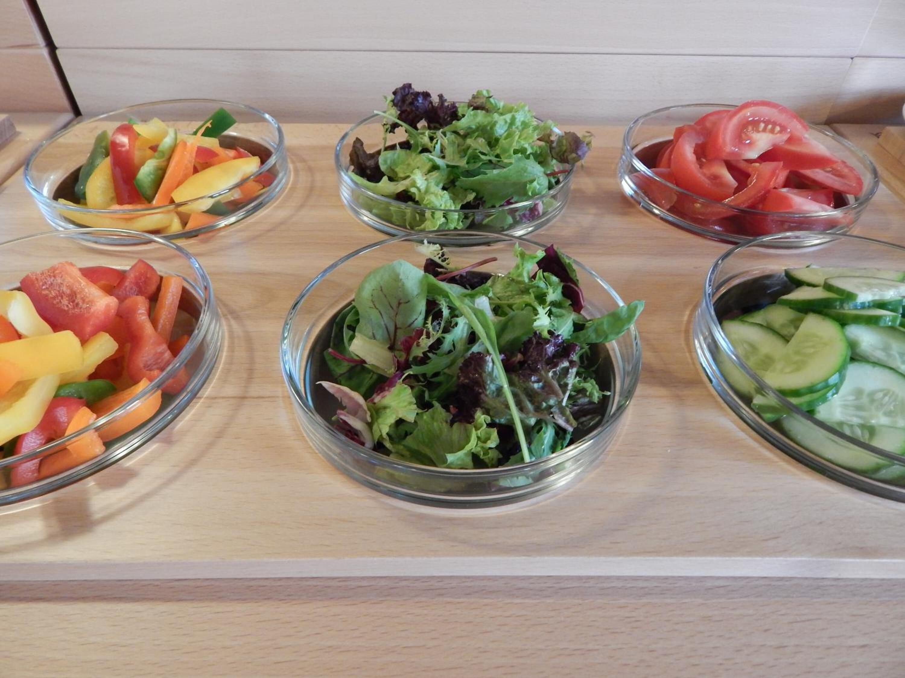 Un bufé con ensaladas variadas, incluyendo verduras mezcladas, lechuga, tomate y pepino.