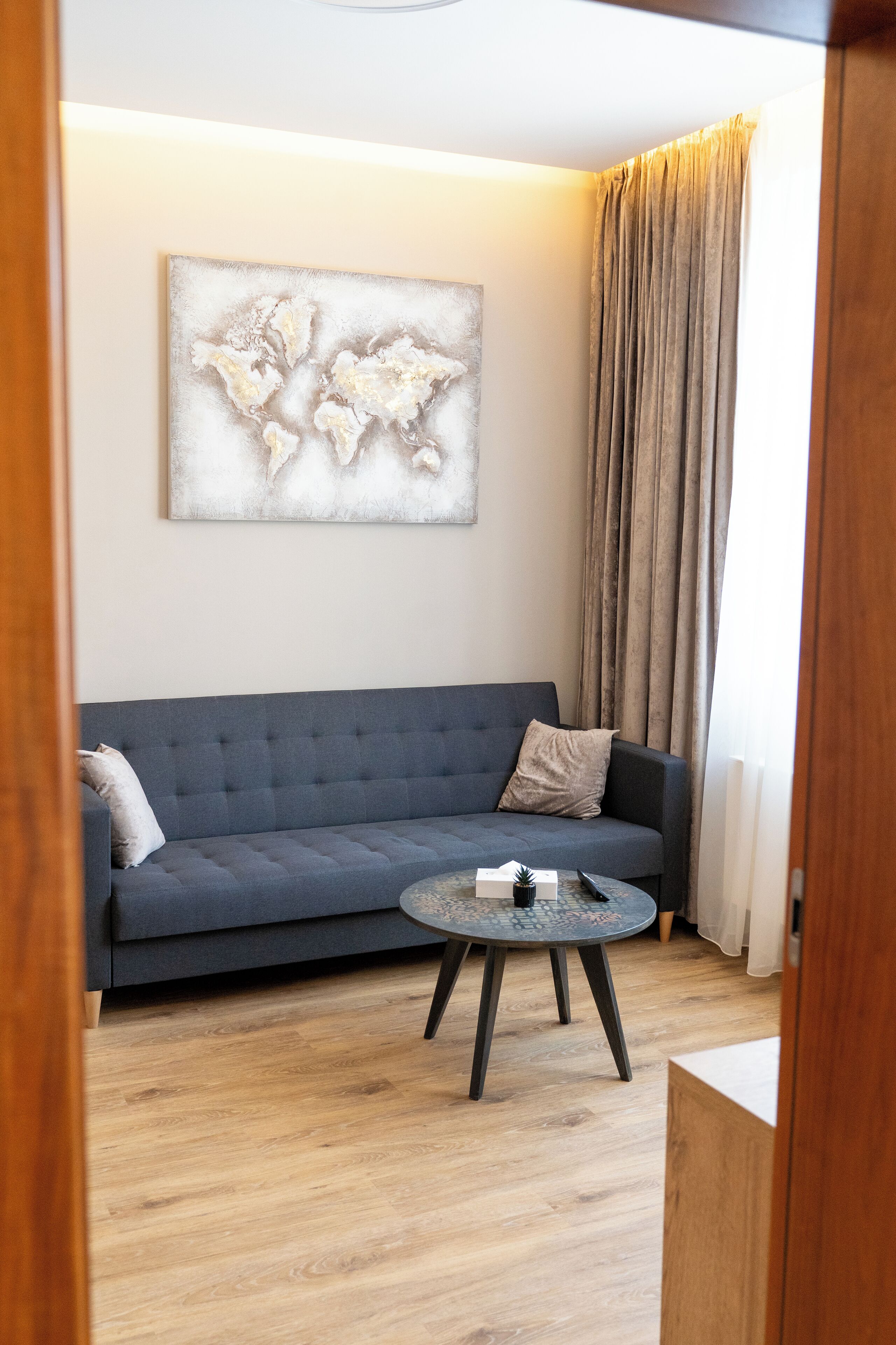 En moderne stue med en grå sofa, et rundt sofabord og et verdenskort som kunst på væggen.