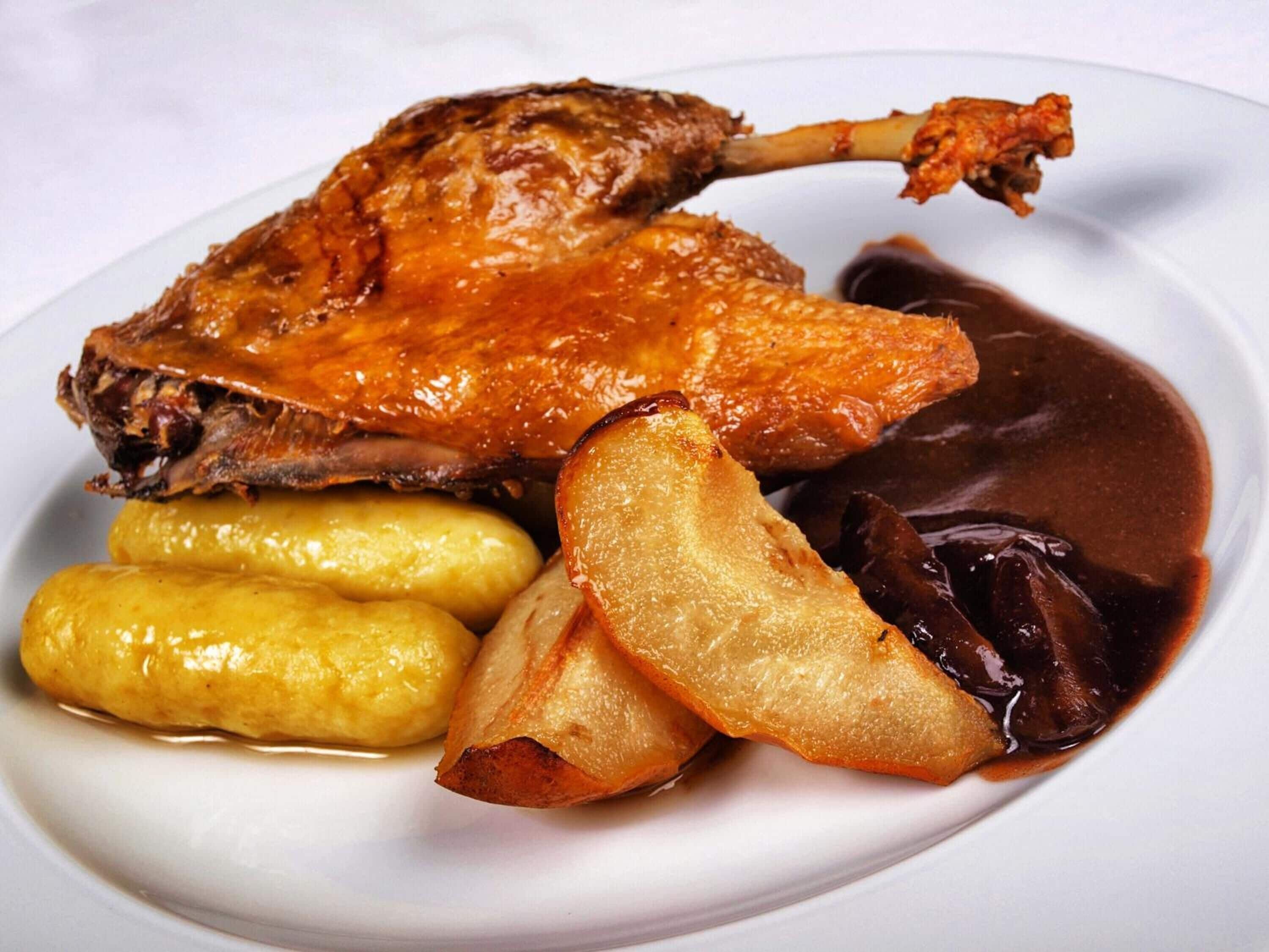 A plate with roasted duck, potatoes, and a dark sauce.