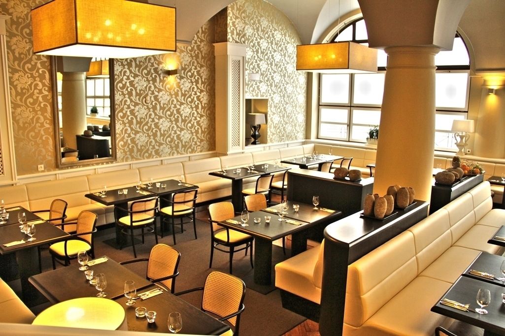 A restaurant with high-backed chairs, dark tables, and a patterned wall.