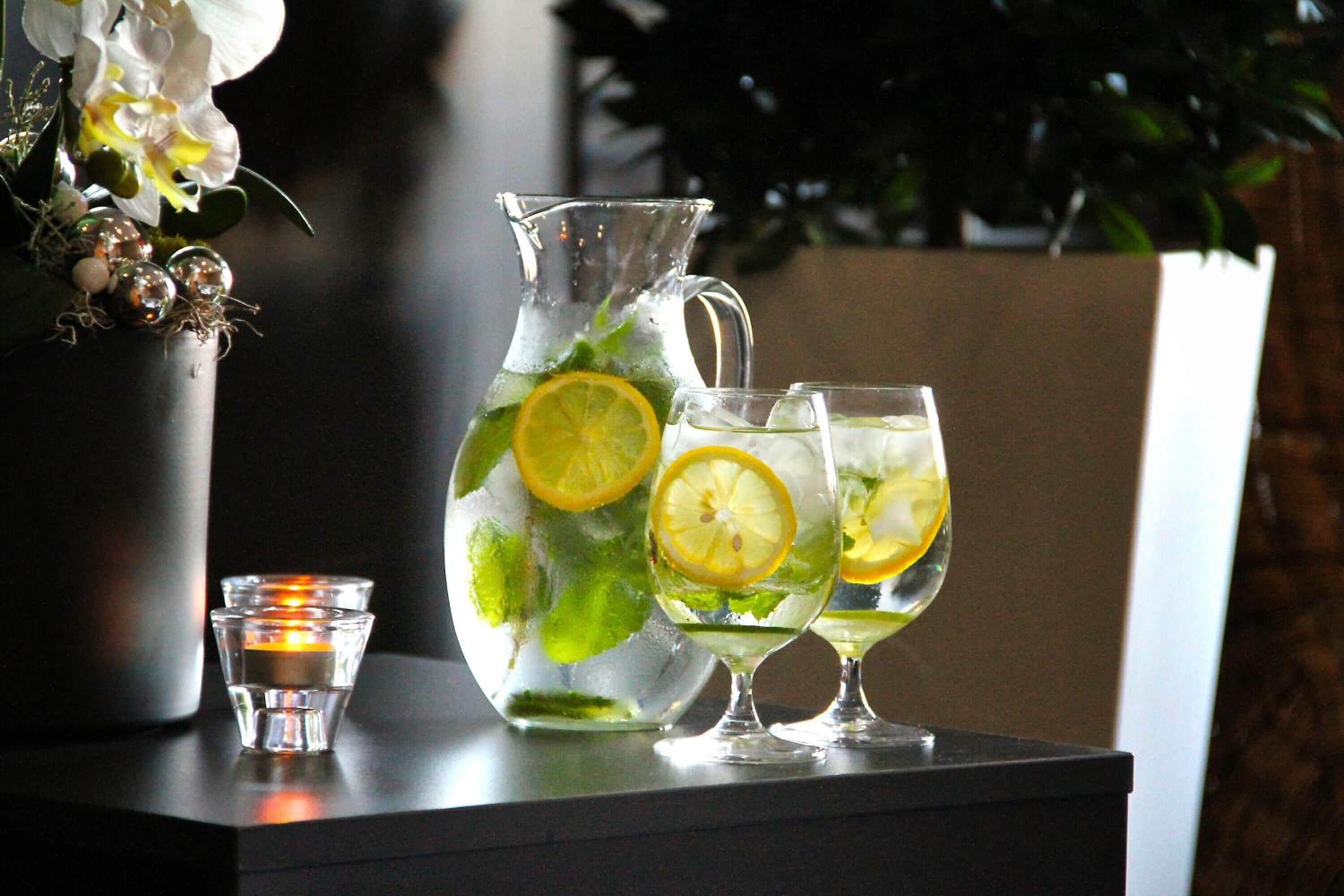 Una jarrón y dos vasos con bebida, una vela y un florero con flores sobre una mesa.
