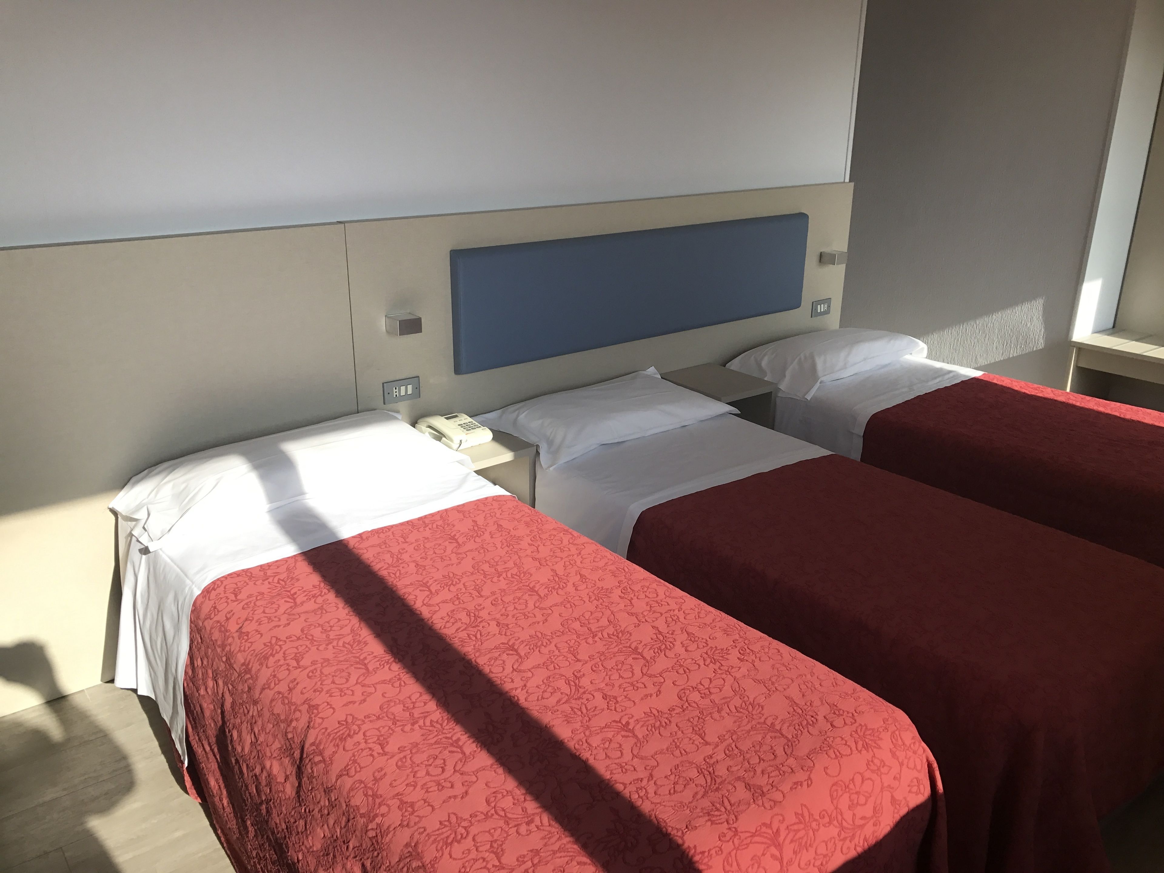 A hotel room with two single beds, a bedside telephone, and a flat-screen TV mounted on the wall.