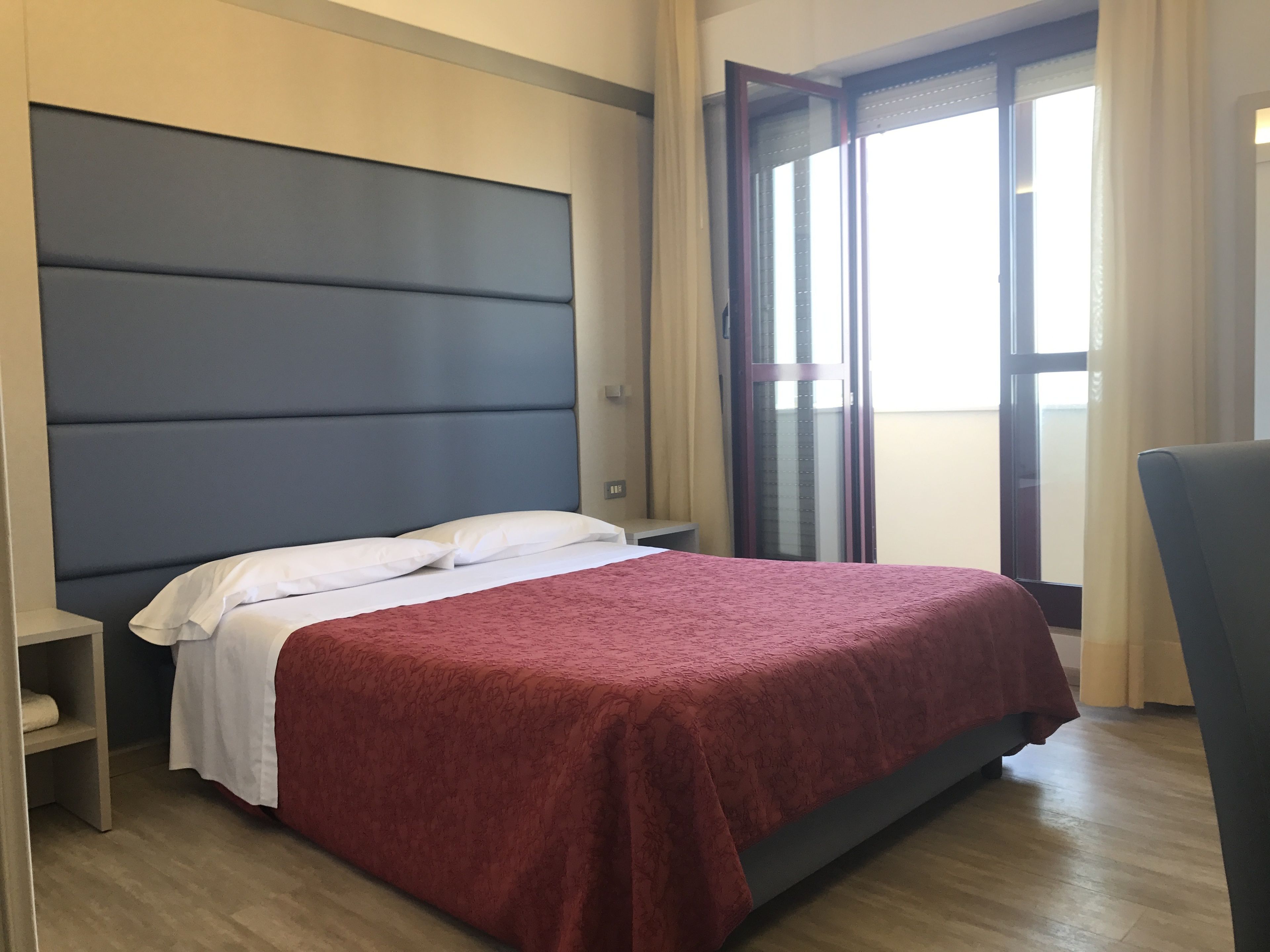 Een moderne hotelkamer met een groot bed, een nachtkastje en een raam met gordijnen.
