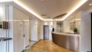 A modern hotel lobby with a reception desk, a staircase, and a door leading to the elevators. - Hotel Elisabeth due (Fano)