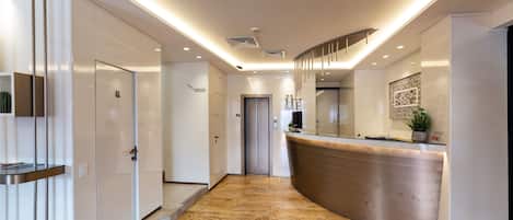 Un moderno vestíbulo de hotel con una recepción, una escalera y una puerta que da acceso a los ascensores.